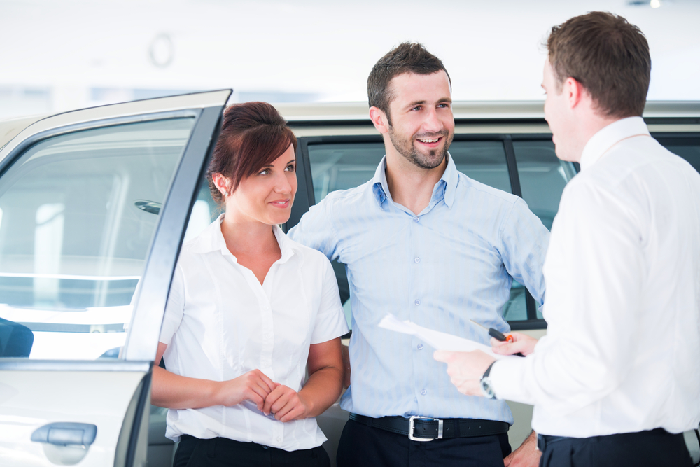 Young couple buying automobile from salesman in a car salon